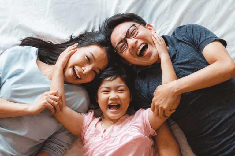 Happy family lying together on a bed, smiling and laughing while spending quality time together at home.