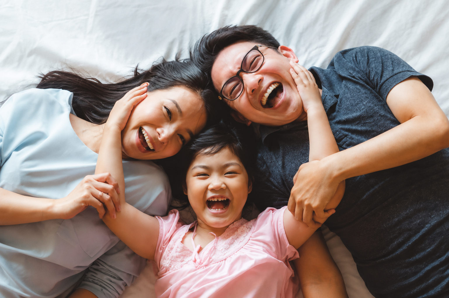 Happy family lying together on a bed, smiling and laughing while spending quality time together at home.